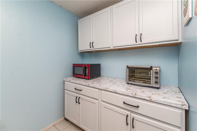 kitchen with light stone countertops, white cabinets, a textured ceiling, and light tile patterned floors