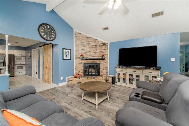 living room with vaulted ceiling with beams, light hardwood / wood-style flooring, a barn door, a fireplace, and ceiling fan