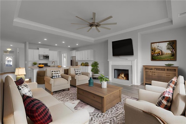 living room with light wood-type flooring, a tray ceiling, ceiling fan, and sink