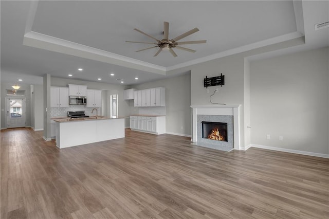 unfurnished living room featuring light hardwood / wood-style floors, ceiling fan, and a tray ceiling