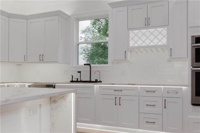 kitchen with light stone counters, decorative backsplash, sink, and white cabinets