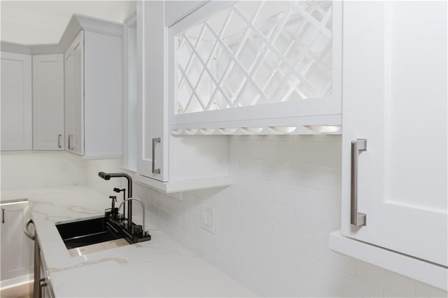 kitchen with white cabinetry, tasteful backsplash, sink, and light stone counters