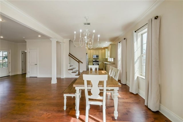 dining area with dark wood-type flooring, crown molding, a notable chandelier, and decorative columns