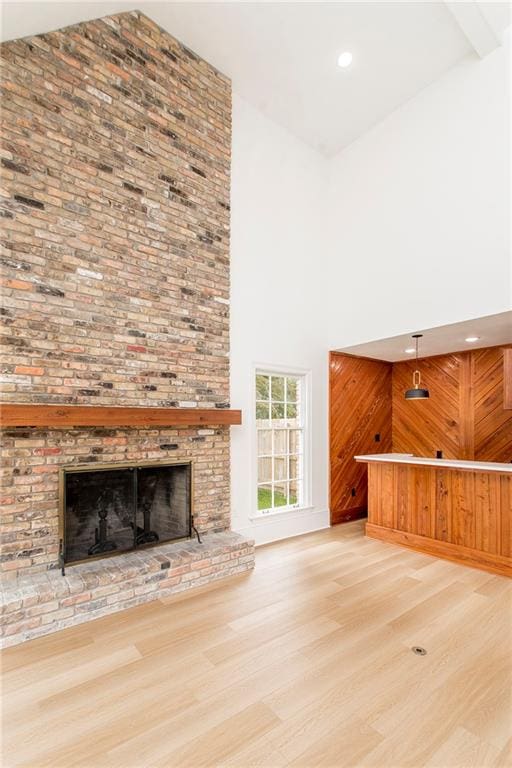 unfurnished living room featuring a brick fireplace, light wood-type flooring, and high vaulted ceiling