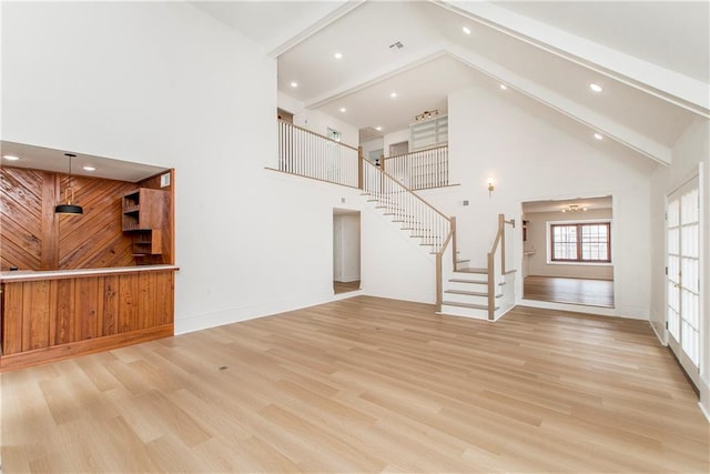 unfurnished living room featuring wood walls, beam ceiling, high vaulted ceiling, and light wood-type flooring