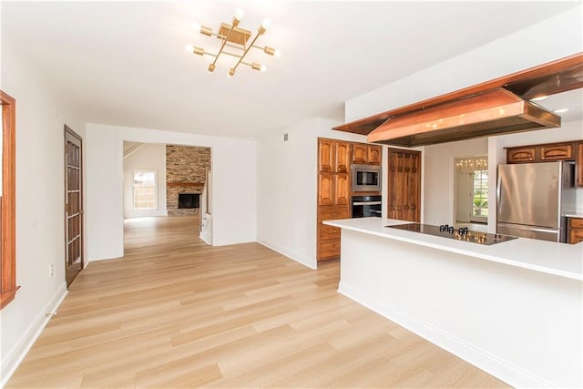 kitchen with stainless steel appliances, a brick fireplace, and light wood-type flooring