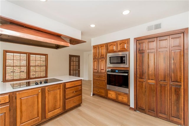 kitchen with light hardwood / wood-style floors, appliances with stainless steel finishes, and beamed ceiling