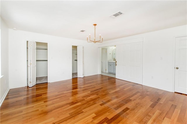 unfurnished bedroom featuring ensuite bath, wood-type flooring, and a chandelier