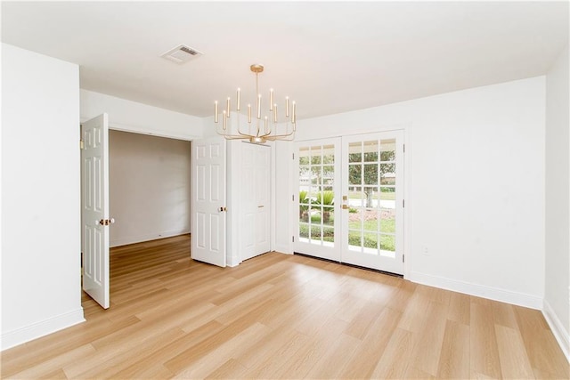 spare room featuring an inviting chandelier, french doors, and light wood-type flooring