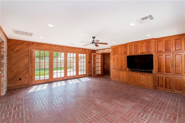 unfurnished living room with french doors, ceiling fan, and wood walls