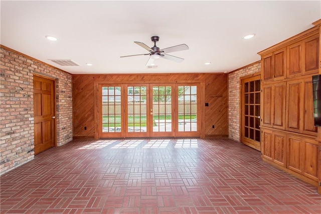 unfurnished living room with brick wall, wooden walls, french doors, and ceiling fan