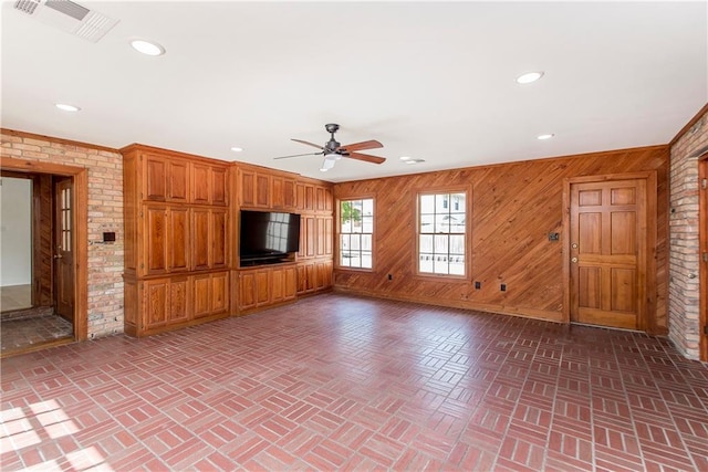 unfurnished living room featuring brick wall, wooden walls, and ceiling fan