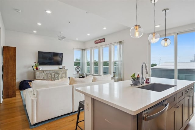 kitchen featuring pendant lighting, sink, an island with sink, light hardwood / wood-style floors, and stainless steel dishwasher