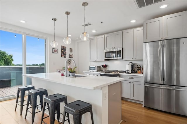 kitchen featuring sink, gray cabinetry, a kitchen island with sink, appliances with stainless steel finishes, and decorative light fixtures