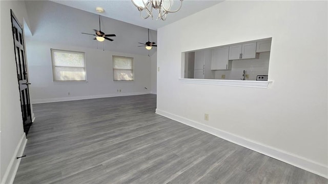 unfurnished living room with ceiling fan with notable chandelier, dark wood-type flooring, and vaulted ceiling