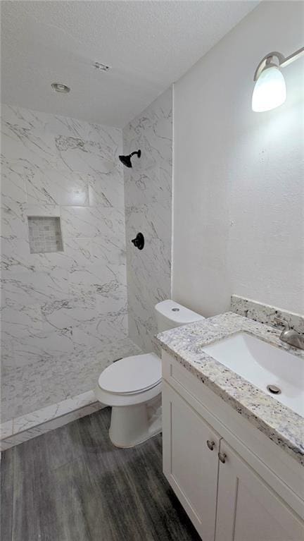 bathroom featuring tiled shower, wood-type flooring, vanity, and toilet