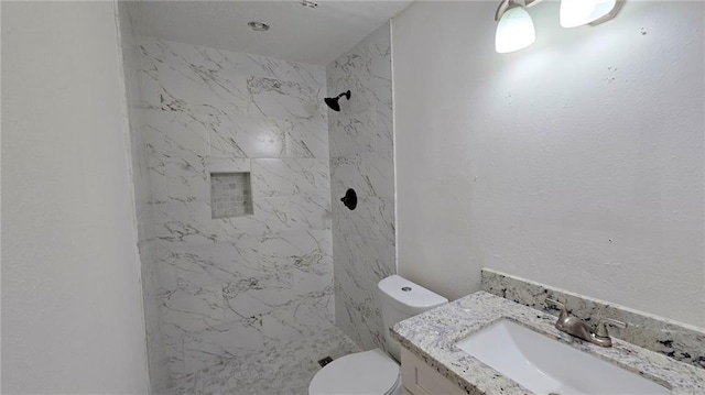 bathroom featuring a tile shower, vanity, and toilet