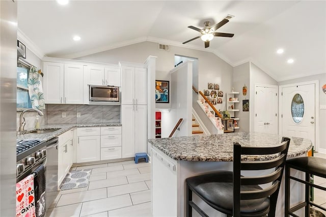 kitchen with lofted ceiling, sink, white cabinets, a breakfast bar, and appliances with stainless steel finishes