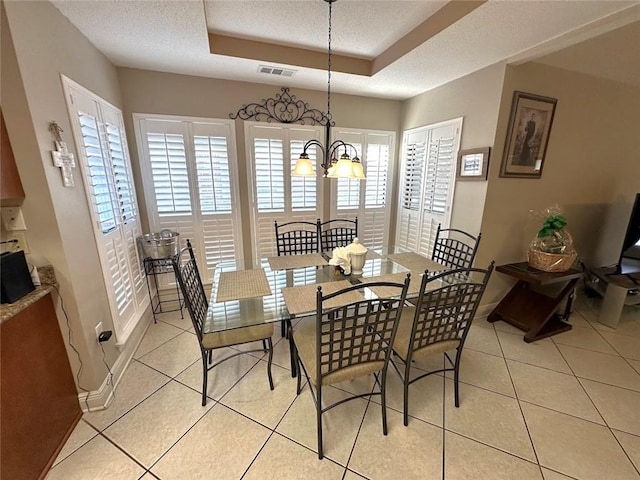 tiled dining area with a textured ceiling, a notable chandelier, and a raised ceiling