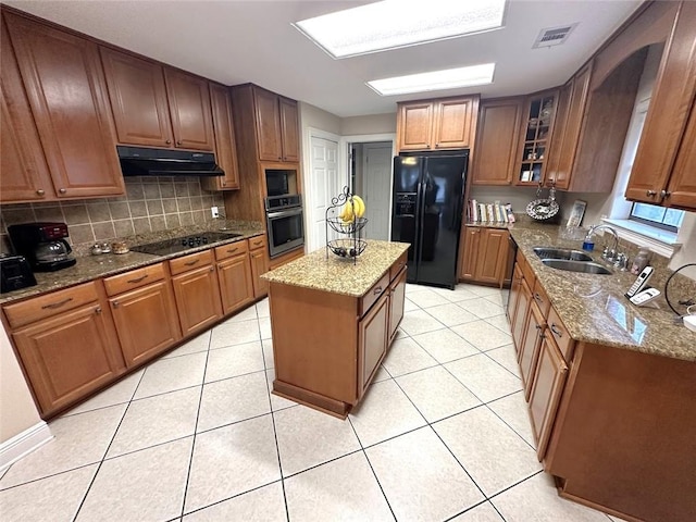 kitchen featuring black appliances, tasteful backsplash, light stone counters, sink, and a center island