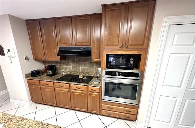 kitchen featuring light tile patterned flooring, black appliances, backsplash, stone counters, and range hood