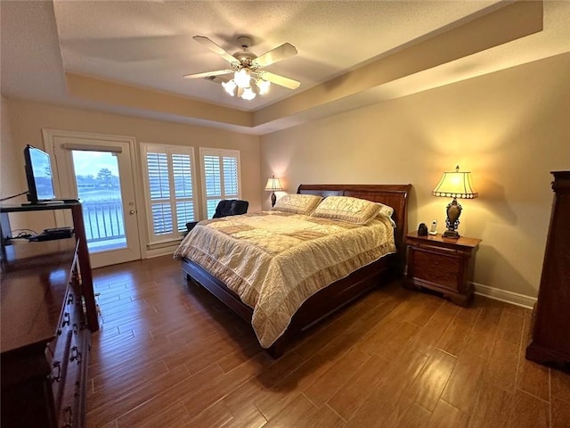 bedroom with dark wood-type flooring, a tray ceiling, ceiling fan, and access to exterior