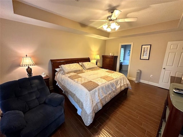 bedroom featuring a raised ceiling, ceiling fan, dark hardwood / wood-style floors, and connected bathroom