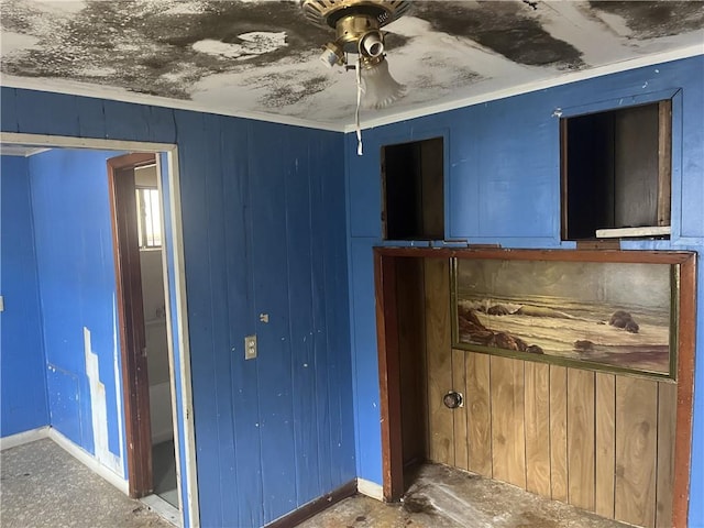 unfurnished bedroom featuring wood walls, crown molding, and ceiling fan