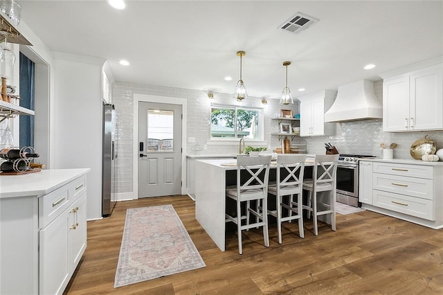 kitchen with hardwood / wood-style floors, white cabinets, appliances with stainless steel finishes, a kitchen island, and custom range hood