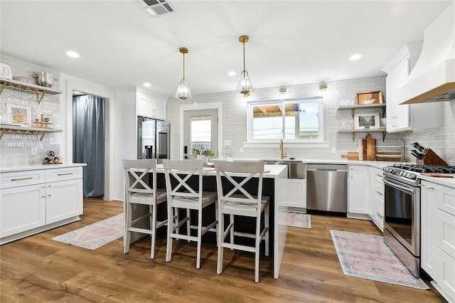 kitchen featuring premium range hood, white cabinets, a kitchen island, and appliances with stainless steel finishes