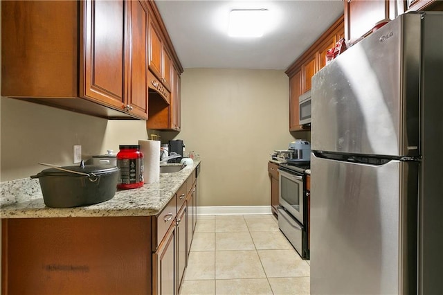 kitchen featuring sink, light stone counters, appliances with stainless steel finishes, and light tile patterned floors