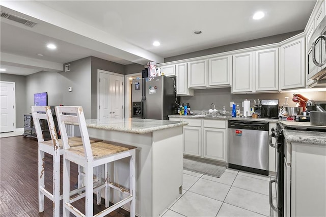 kitchen with light stone countertops, appliances with stainless steel finishes, a center island, light hardwood / wood-style floors, and white cabinets