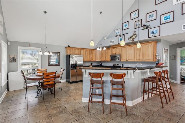 kitchen featuring decorative light fixtures, stainless steel appliances, dark countertops, an inviting chandelier, and a kitchen breakfast bar