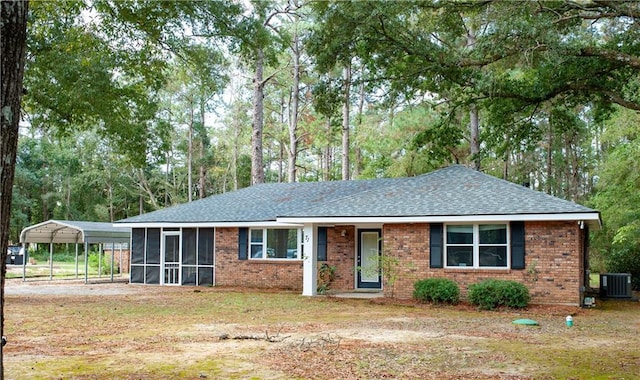 ranch-style house featuring a detached carport, a front yard, a sunroom, brick siding, and central AC unit