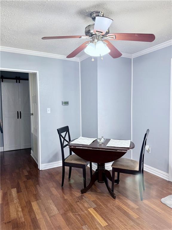 dining space with baseboards, wood finished floors, a textured ceiling, and ornamental molding