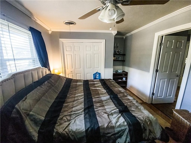 bedroom with wainscoting, crown molding, visible vents, and a closet