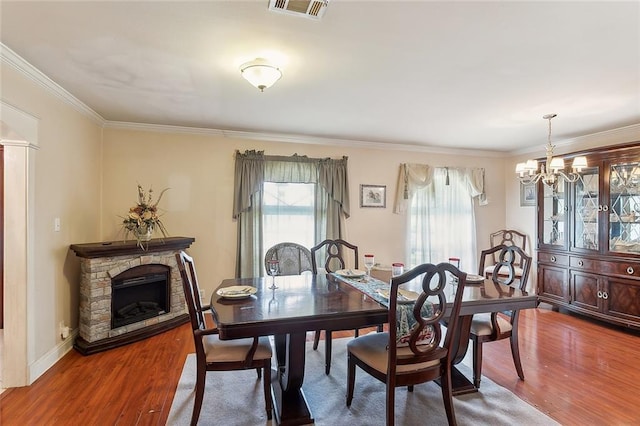 dining space with ornamental molding, hardwood / wood-style floors, a notable chandelier, and a fireplace