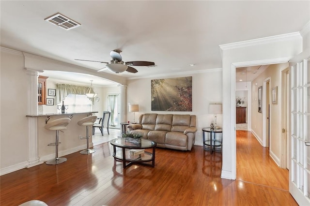 living room featuring decorative columns, ceiling fan, hardwood / wood-style flooring, and ornamental molding