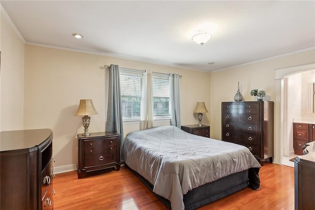 bedroom with connected bathroom, light hardwood / wood-style floors, and ornamental molding