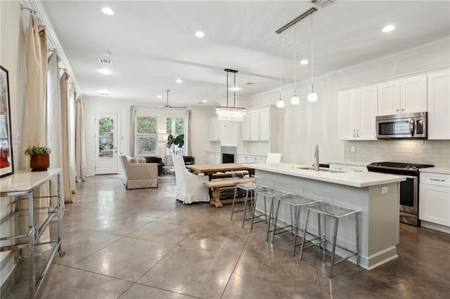 kitchen featuring a center island with sink, white cabinetry, hanging light fixtures, and stainless steel appliances