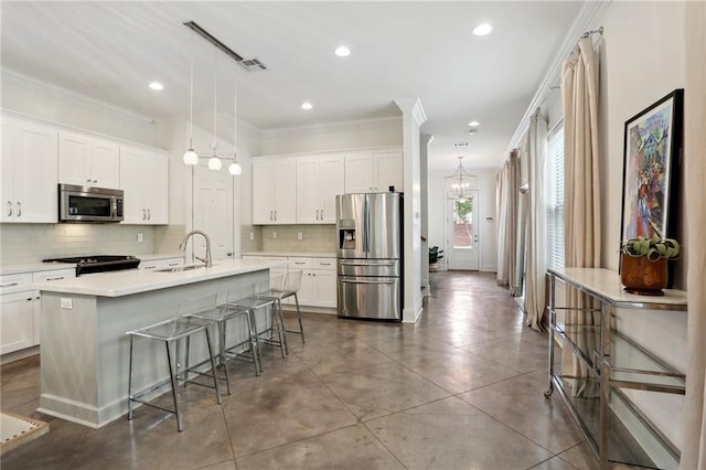 kitchen featuring white cabinets, hanging light fixtures, an island with sink, appliances with stainless steel finishes, and a breakfast bar