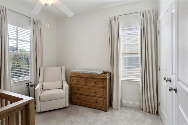 bedroom with ceiling fan, multiple windows, a crib, and light colored carpet