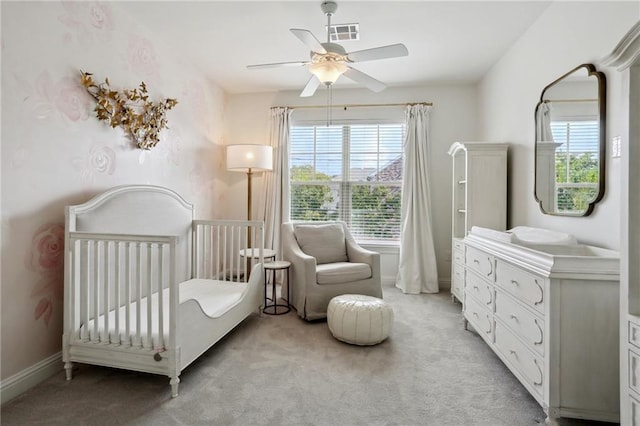 carpeted bedroom with multiple windows, a crib, and ceiling fan