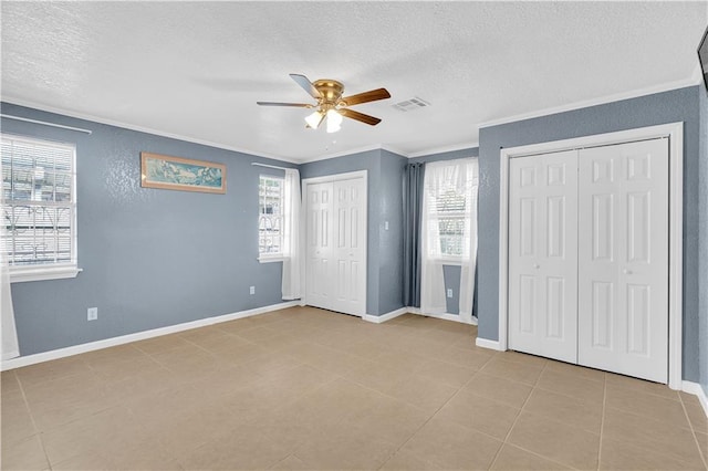 unfurnished bedroom featuring ornamental molding, a textured ceiling, two closets, and ceiling fan