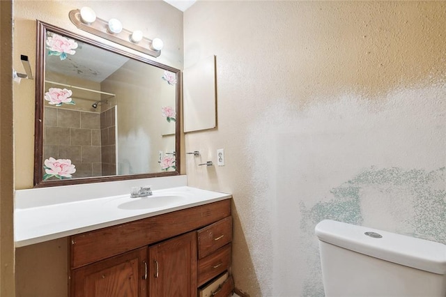 bathroom with toilet, vanity, and tiled shower