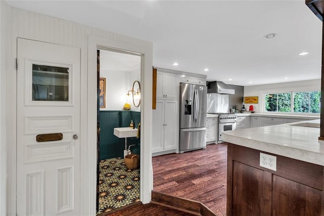 kitchen featuring dark hardwood / wood-style flooring, appliances with stainless steel finishes, white cabinetry, wall chimney exhaust hood, and sink