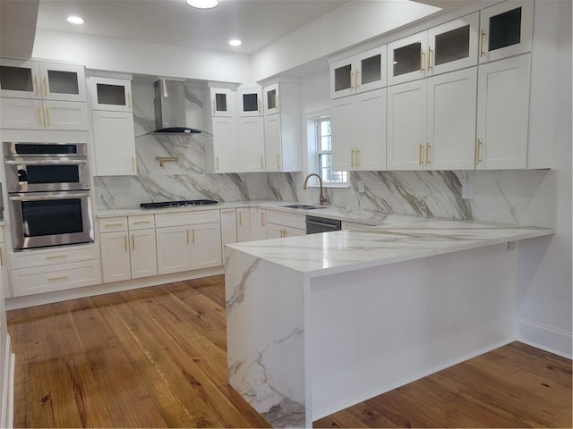 kitchen featuring appliances with stainless steel finishes, light stone countertops, white cabinets, wall chimney range hood, and decorative backsplash