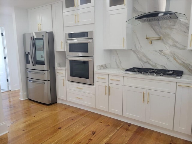 kitchen featuring extractor fan, light wood-type flooring, stainless steel appliances, and white cabinets