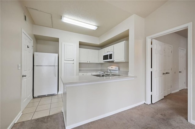 kitchen with white appliances, light carpet, white cabinets, sink, and kitchen peninsula