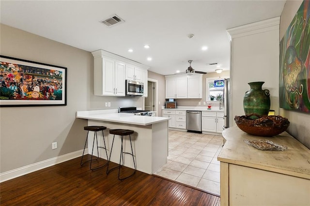 kitchen with light wood-type flooring, kitchen peninsula, white cabinetry, stainless steel appliances, and a breakfast bar area